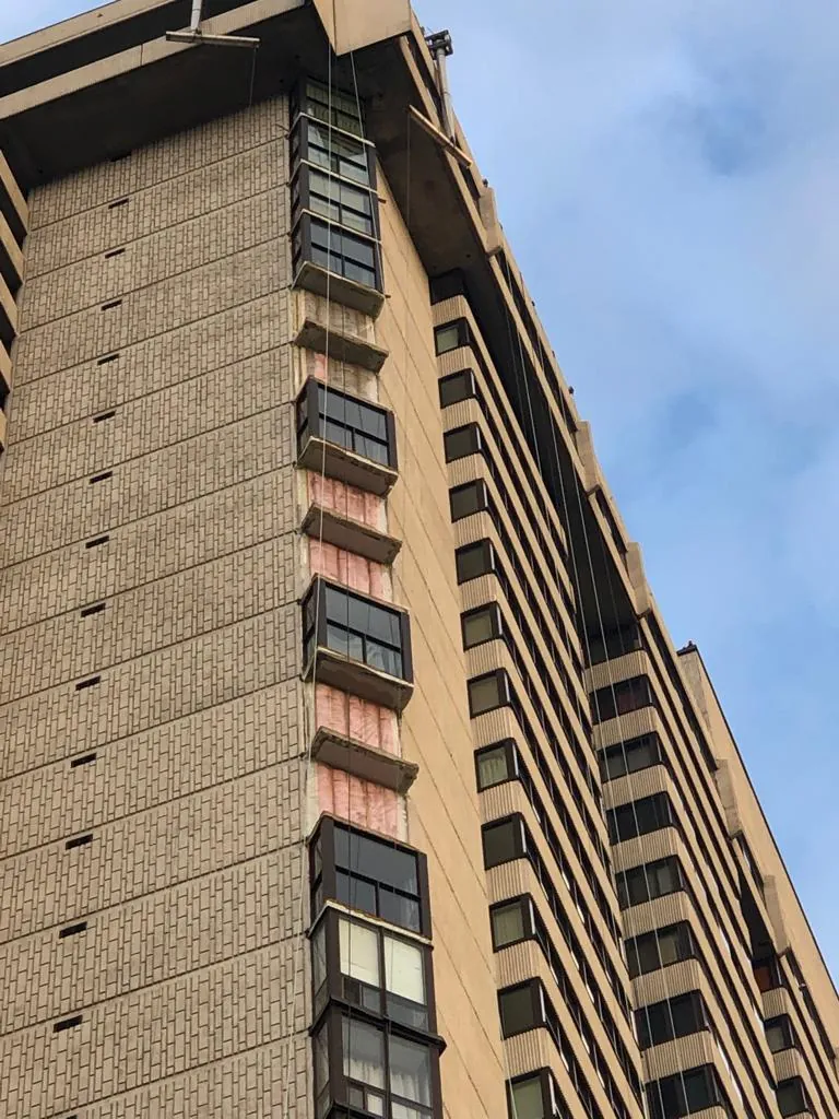 Tower bay windows removed, insulation exposed, rigging lines down the face
